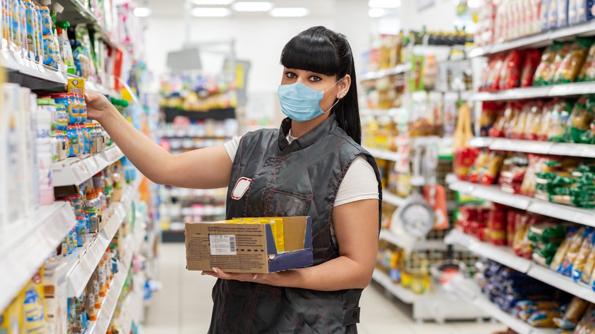 Coronavirus. Seller a woman in a medical mask puts the product on the shelves. The concept of protection from the virus