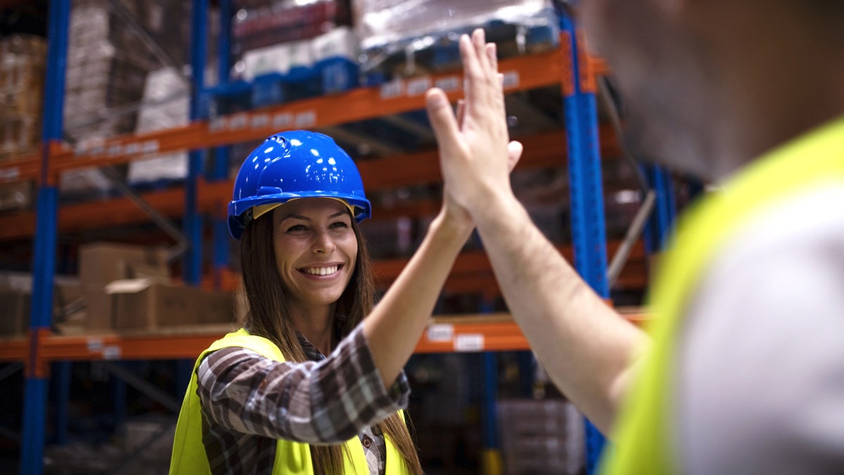 Zwei ArbeiterInnen in Warnwesten und mit Schutzhelm geben sich ein High-Five