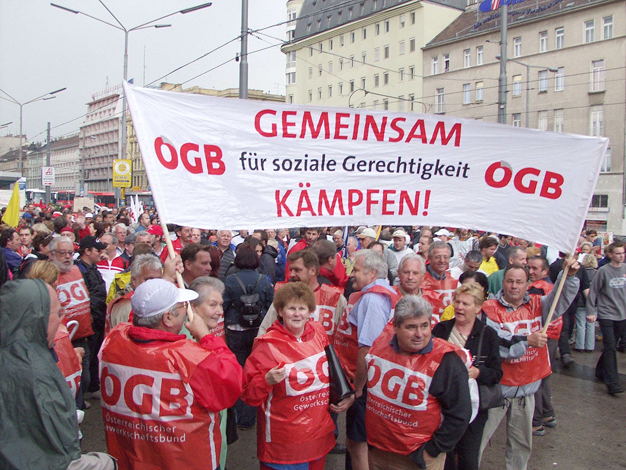 Am 13. Mai 2003 demonstrierten rund 200.000 Menschen gegen die Pensionsreform. Am Bild ist ein Banner: ÖGB, Gemeinsam für soziale Gerechtigkeit. Frauen und Männer tragen roten Regenschutz mit ÖGB-Aufdruck