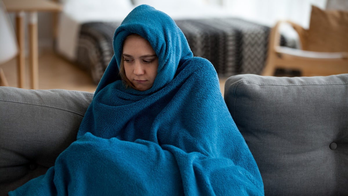 Woman feeling cold covered with warm blanket at home