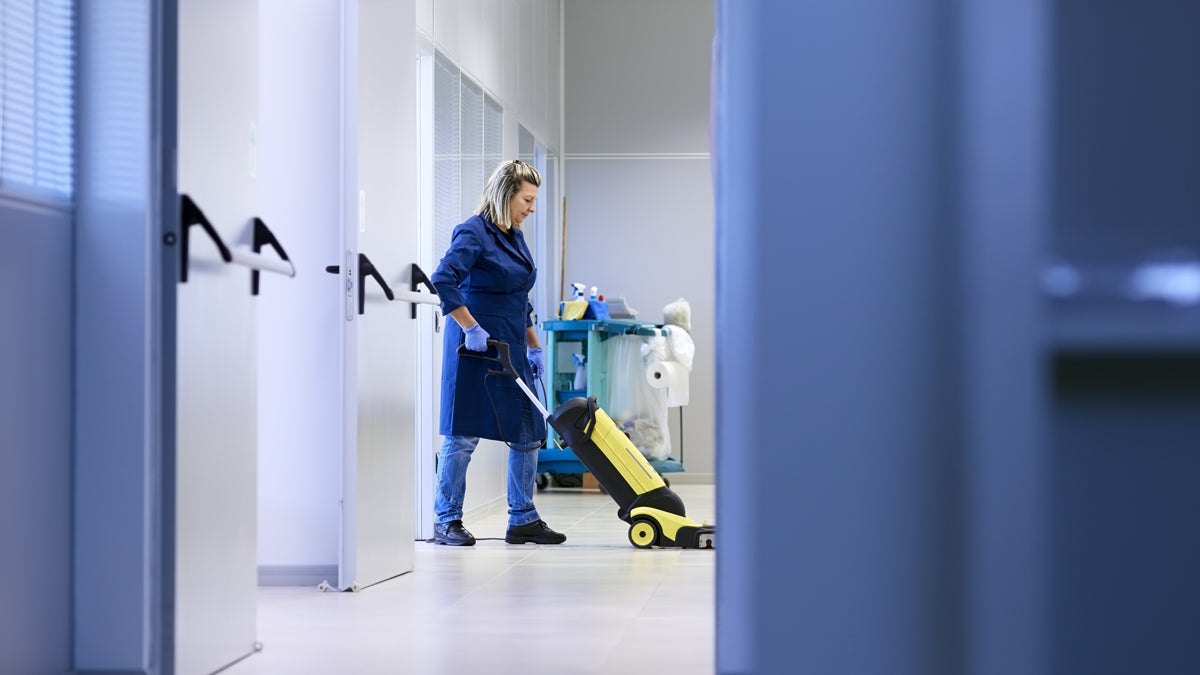 Reinigungskraft säubert Boden mit Maschine in Bürogebäude