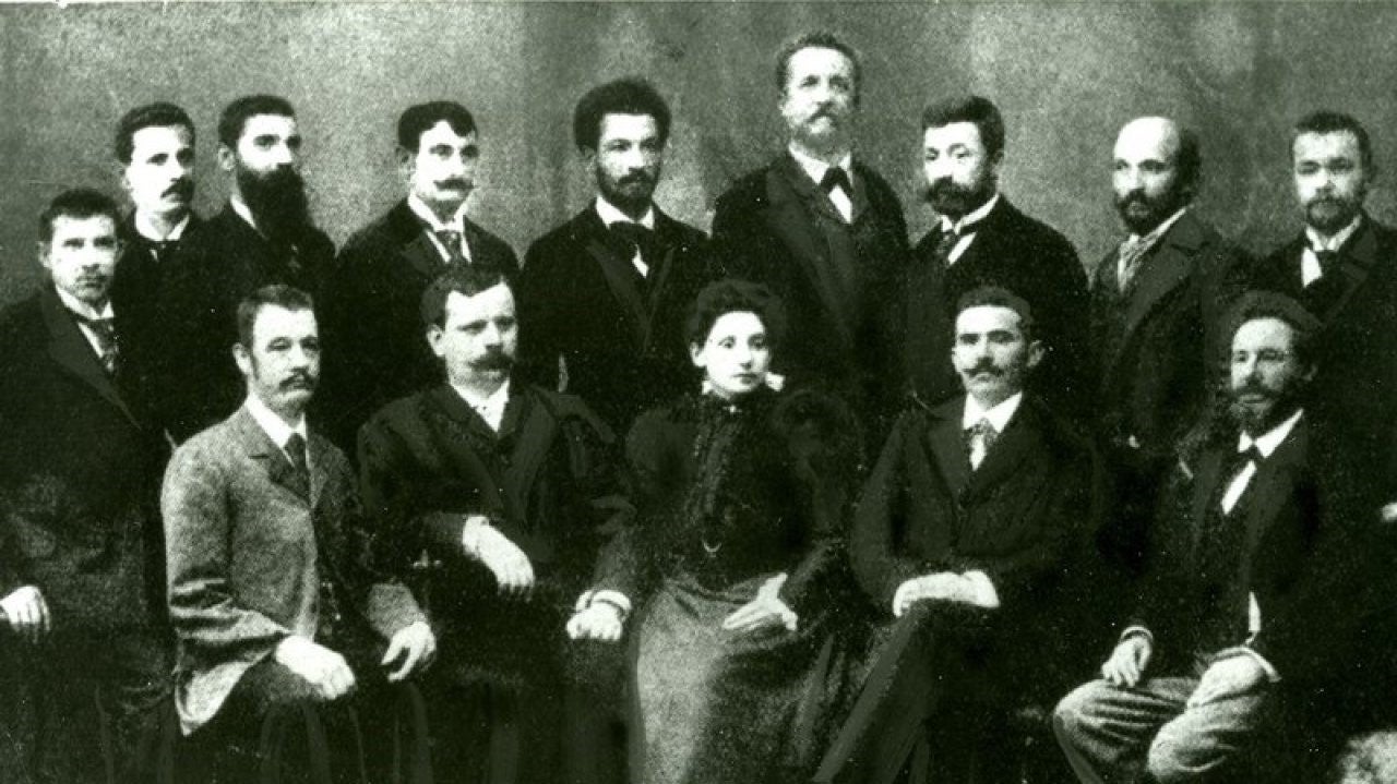 Eine Gruppe von Männern mit beeindruckenden Bärten und vorne sitzend Anna Boschek mit langem Kleid.  