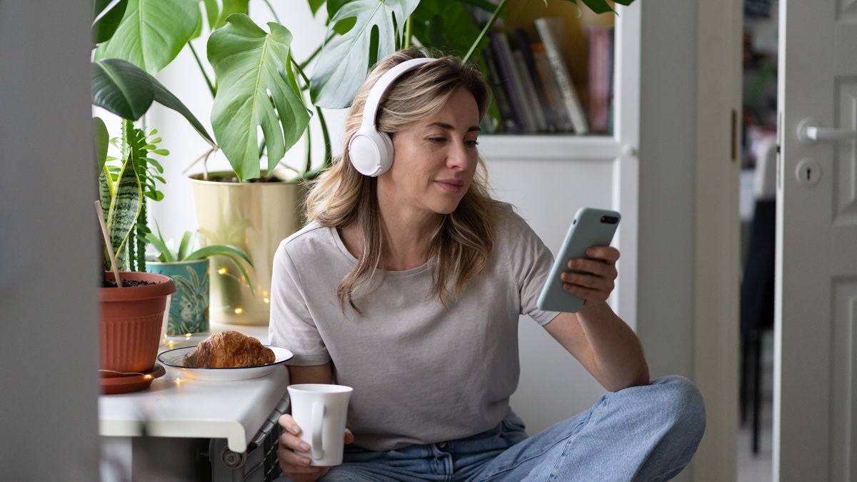 Frau sitzt in ihrere Wohnung mit einer Tasse Kaffee und hört Podcasts über Kopfhörer