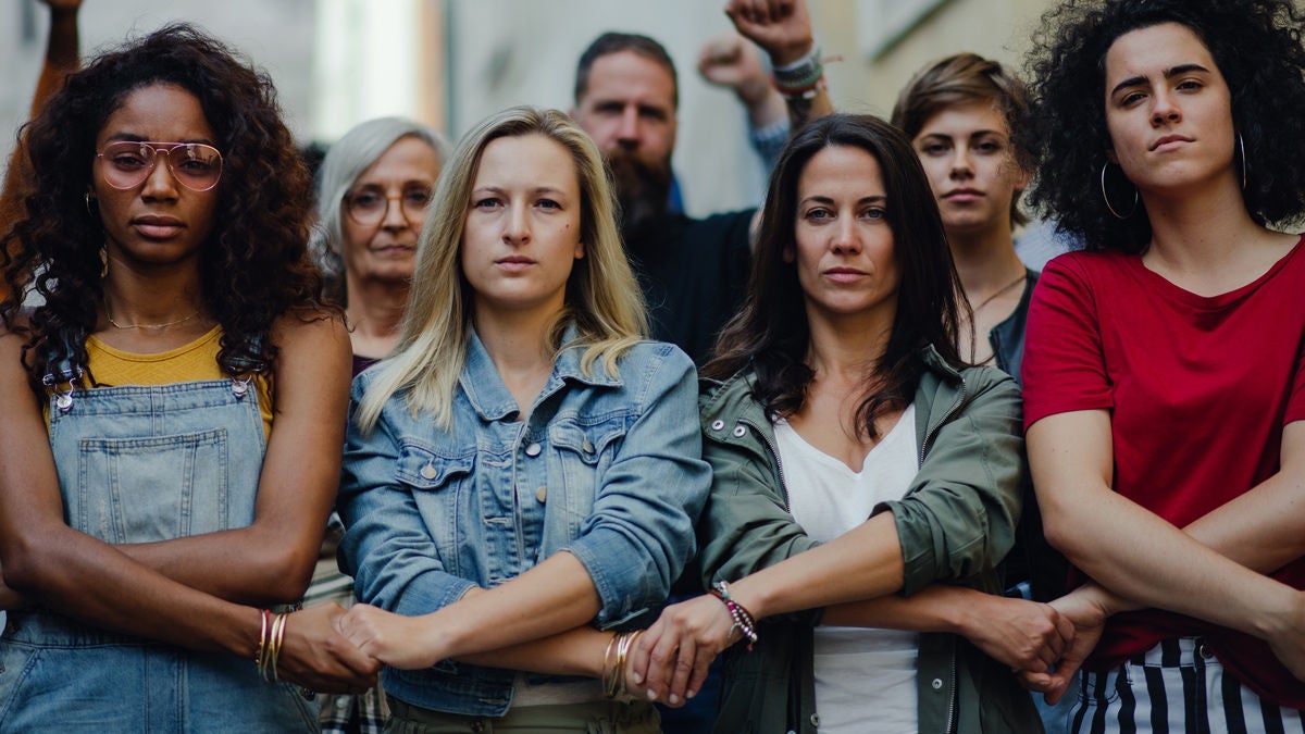 Gruppe reicht sich die Hände auf einer Demonstration und schaut kämpferisch in die Kamera