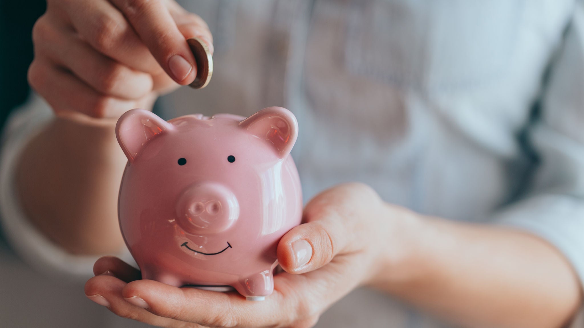 female hands puts a coin in a pink piggy bank. The concept of saving money or savings, investment