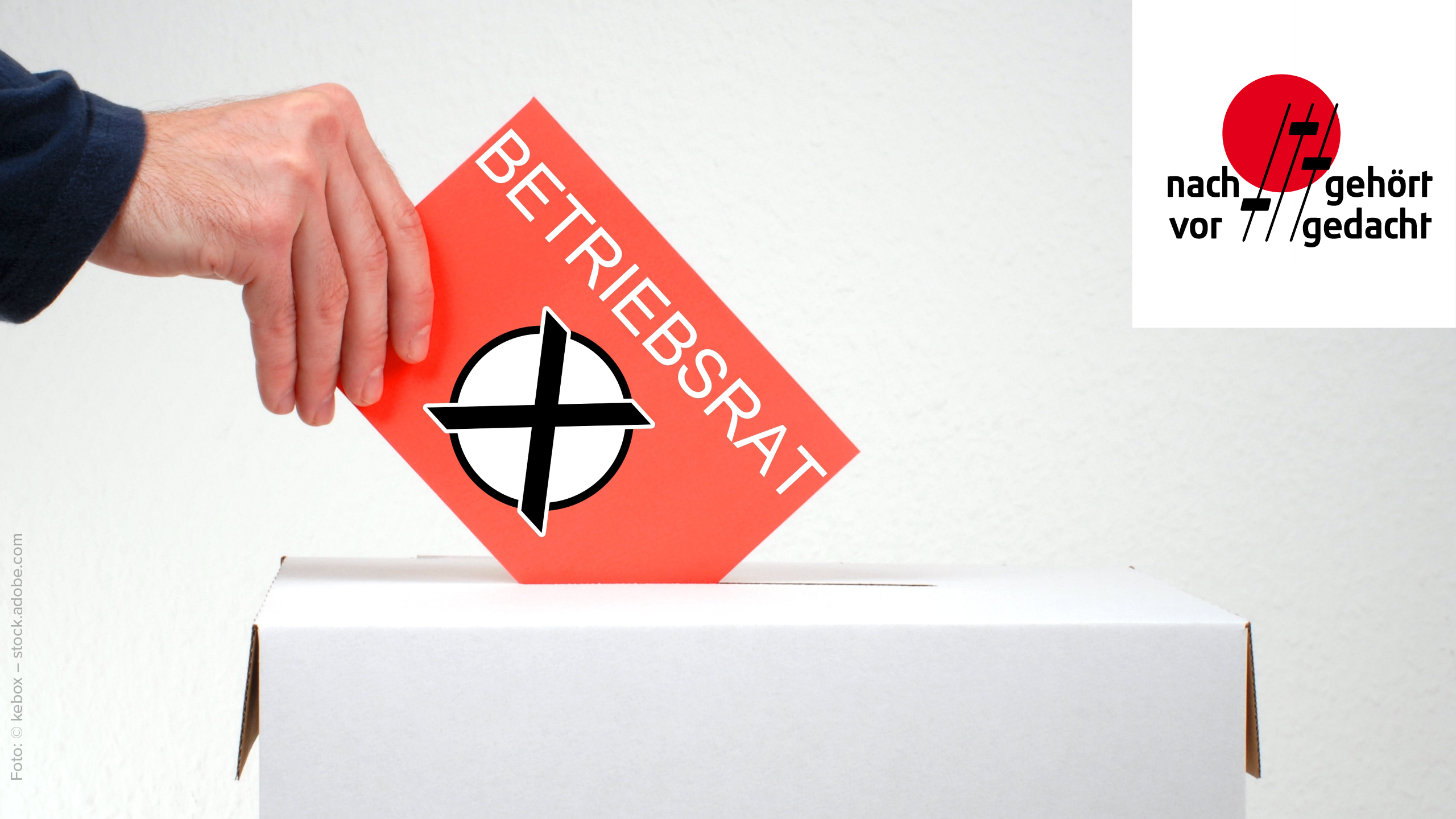 Hand wirft Stimmzettel mit Aufschrift "Betriebsrat" in Wahlurne. 