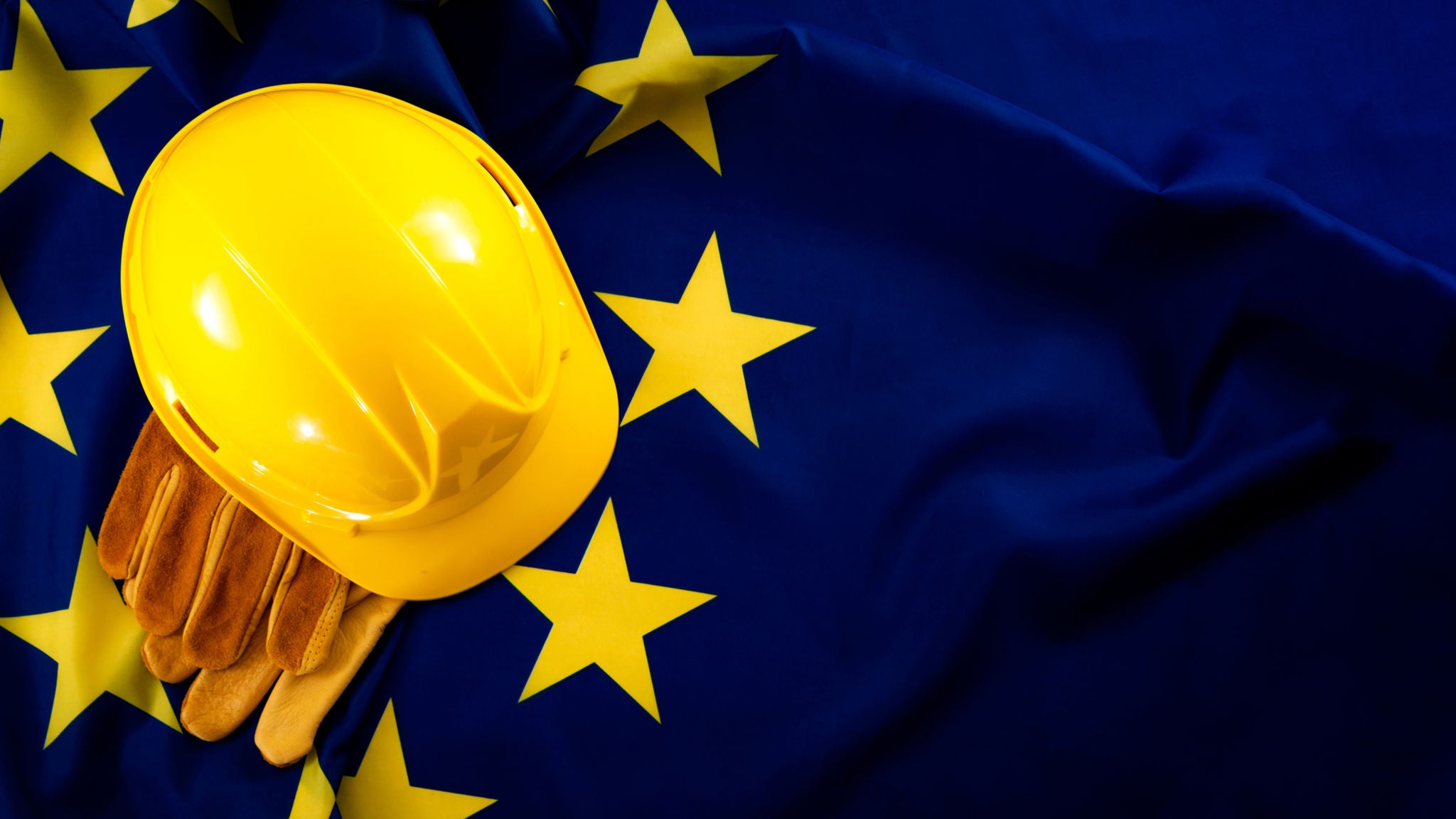 Gelber Schutzhelm und Arbeitshandschuhe auf einer Flagge der Europäischen Union.