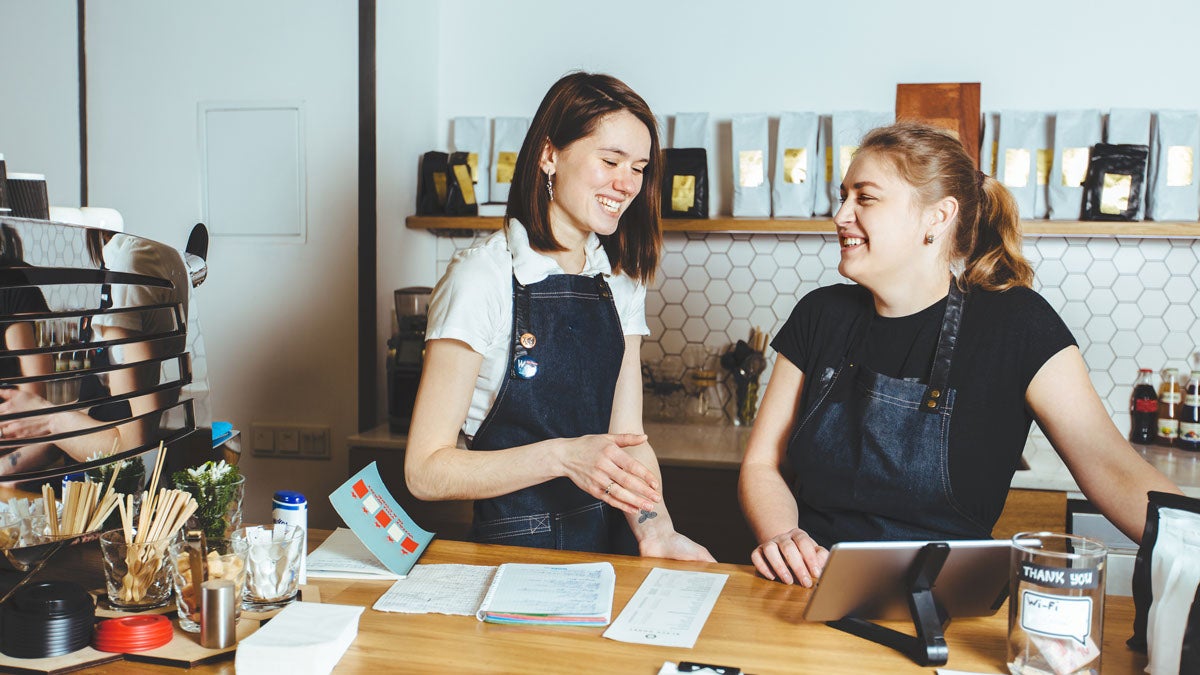 Zwei junge, fröhliche Barista stehen hinter der Theke und unterhalten sich.