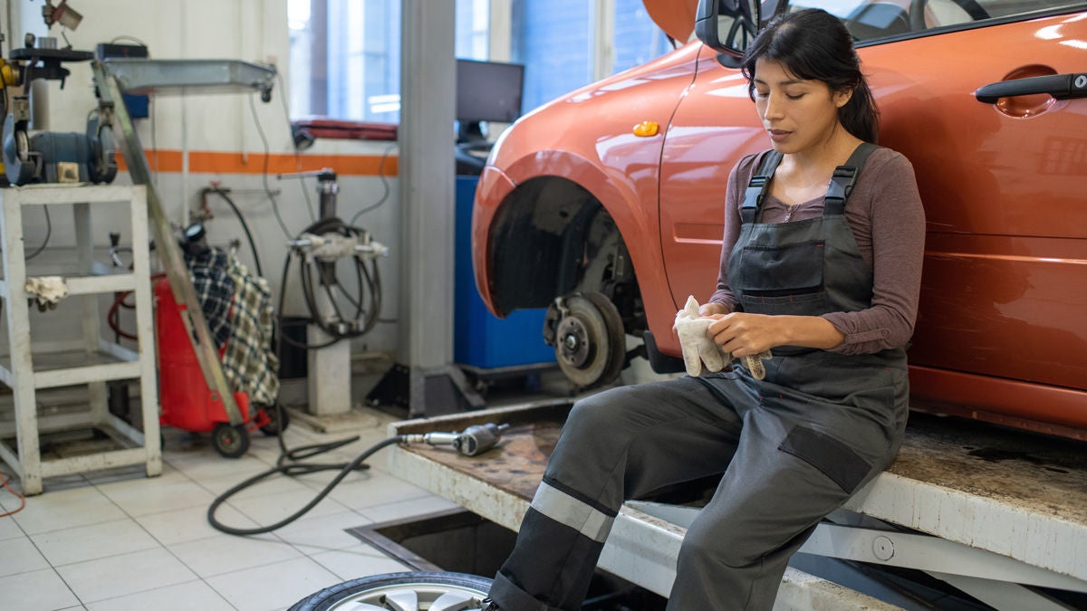 Mechanikerin sitzt auf der Hebebühne und arbeitet an einem Auto