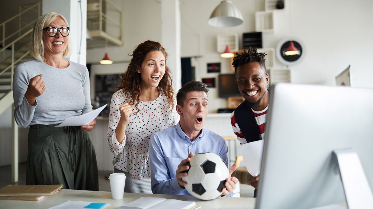 Gruppe von KollegInnen sitzen vorm Computer und schauen ein Fußball-Match