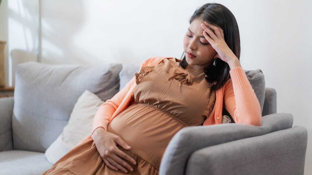Eine schwangere Frau sitzt sorgenvoll in ihrer Wohnung