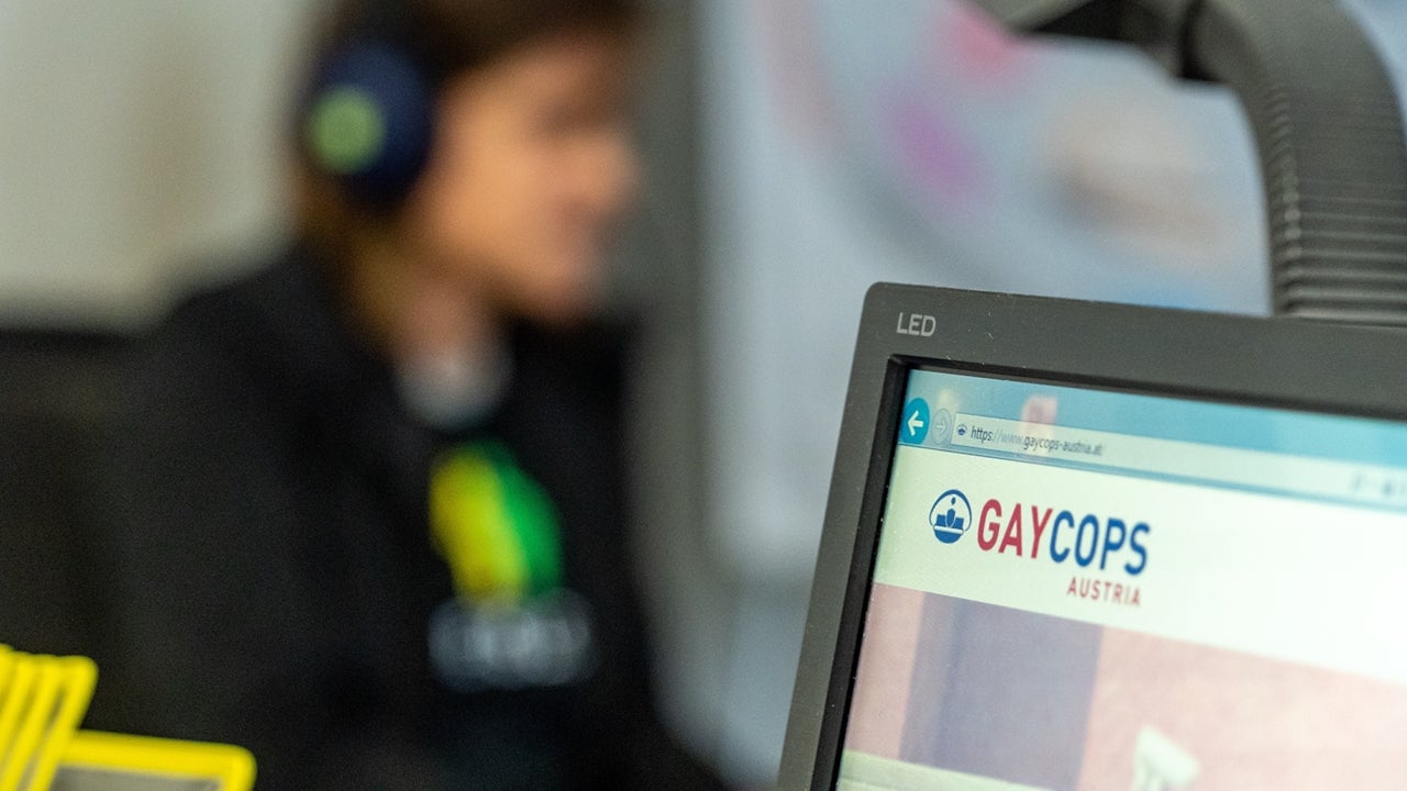 Gay Cops Austria Compterbildschirm mit dem Logo der Gay Cops Austria im Vordergrund, im Hintergrund verschwommen die Vorsitzende Christina Gabriel