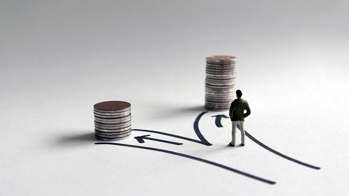 Miniatur Figur steht vor zwei ungleich hohen Münzstapeln, am Boden ist eine Wegkreuzung aufgezeichnet