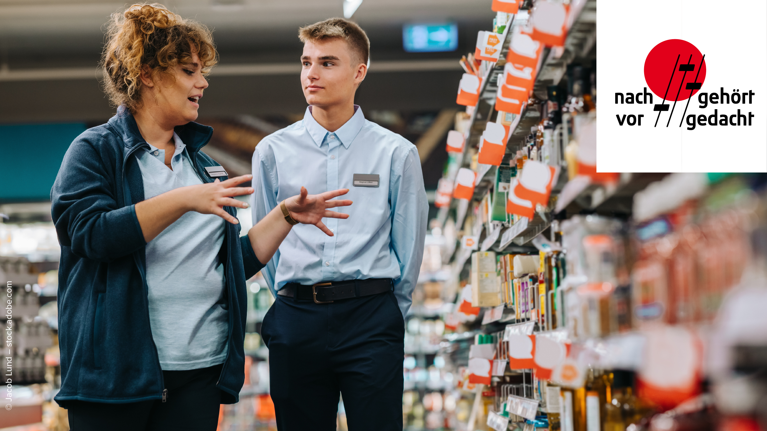Supermarkt Managerin erklärt Lehrling etwas während sie beide vor einem Regal stehen. Das Regal und der Hintergrund sind unscharf, Produkte sind nicht zu erkennen. In der rechten oberen Ecke ist das "nachgehört - vorgedacht" Podcast Logo platziert