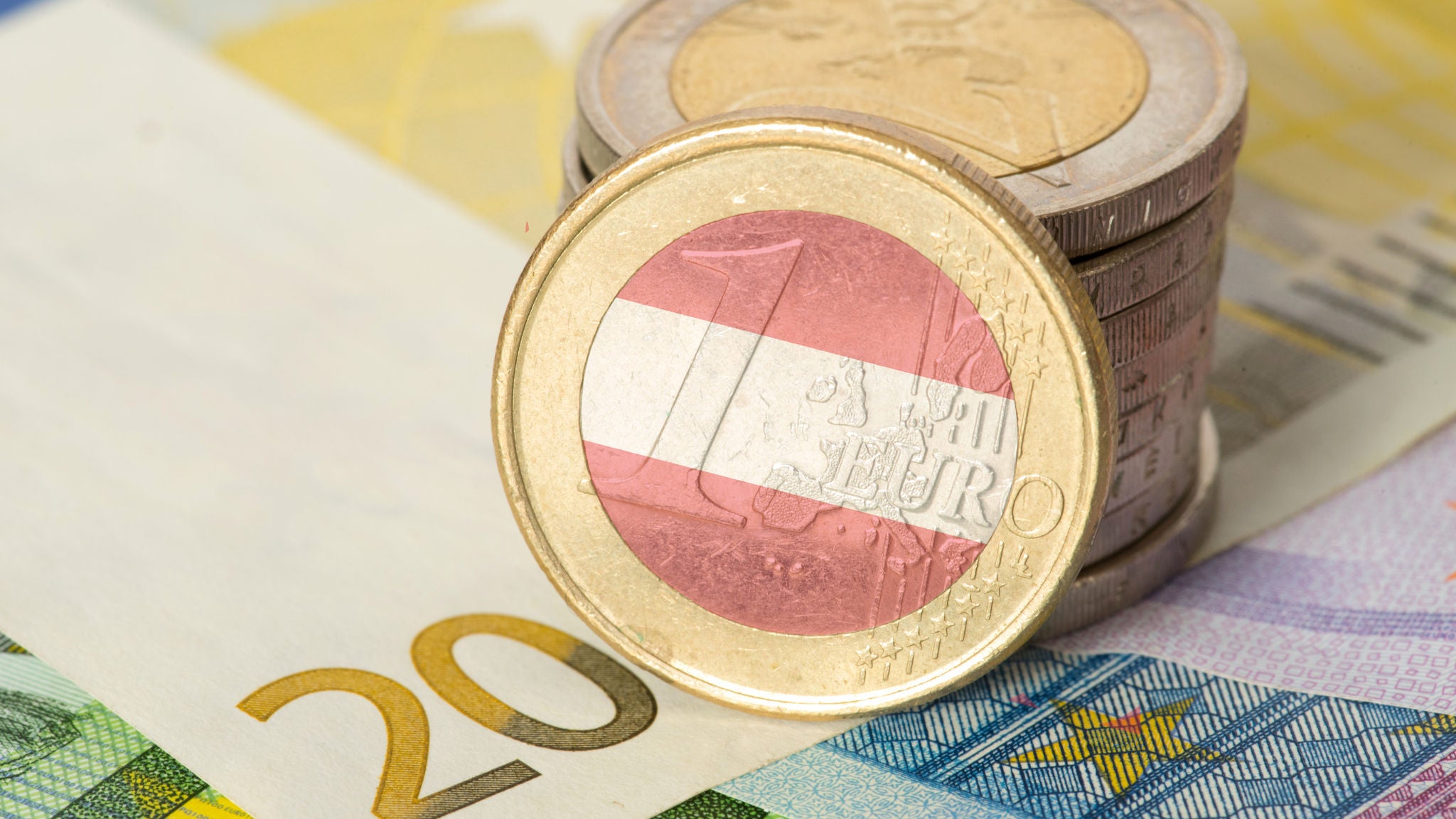 1-Euro-Münze mit österreichischer Flagge vor gestapelten Euromünzen und Euro-Banknoten