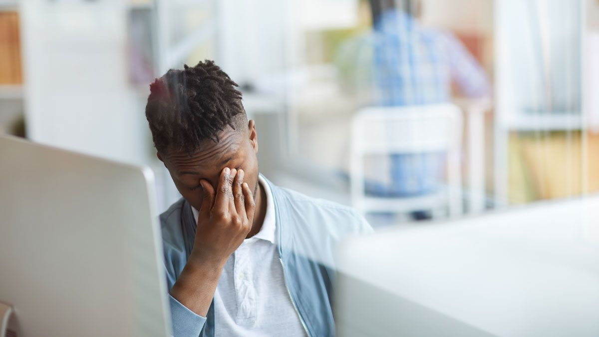 Mann sitzt an seinem Schreibtisch und reibt sich müde und frustriert die Augen
