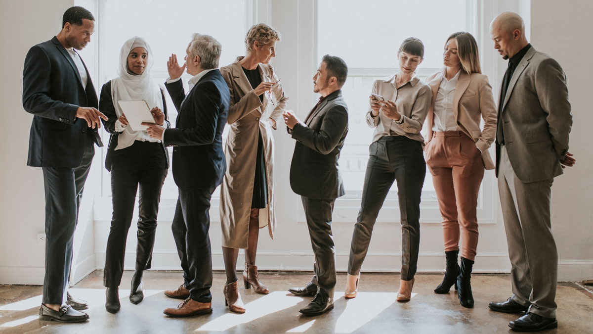 Diverse Gruppe an Menschen in Bürokleidung, steht zusammen und unterhält sich.