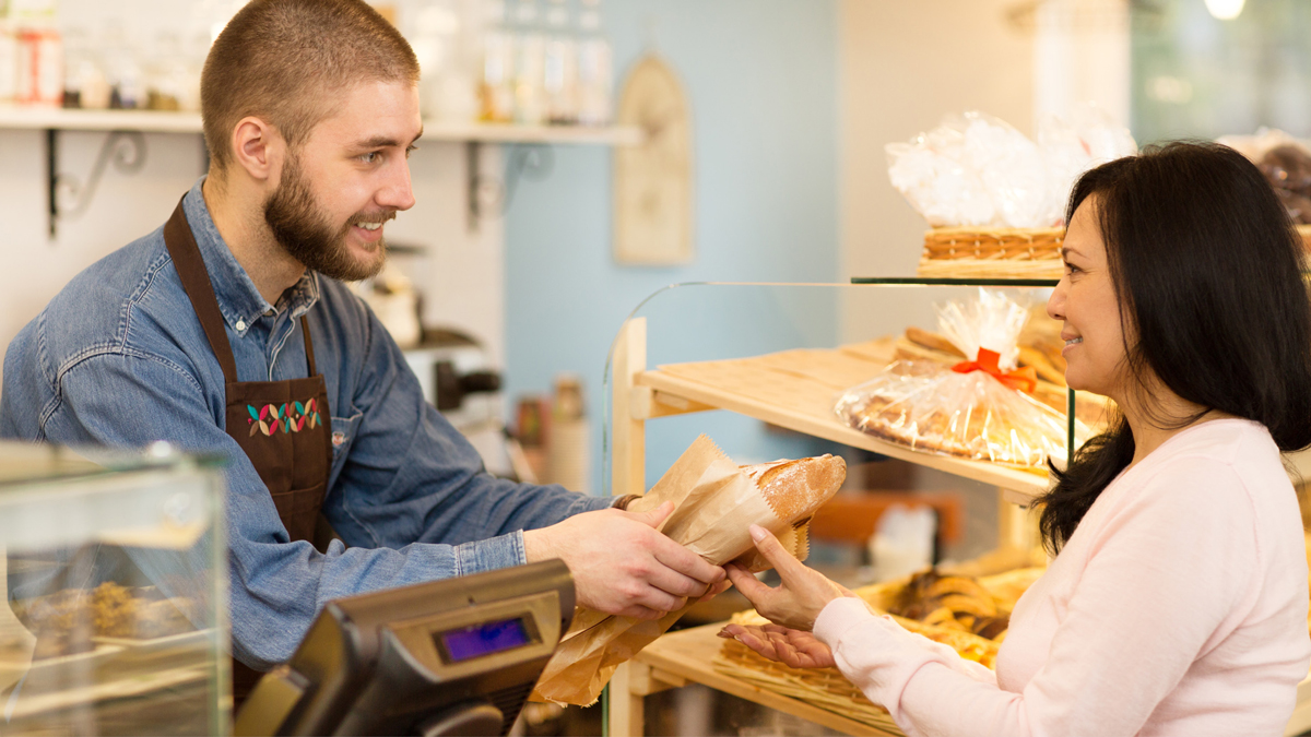 Einzelhandel Bäckerei Verkäufer in einer Bäckerei reicht Kundin ihr in Papier verpacktes Brot