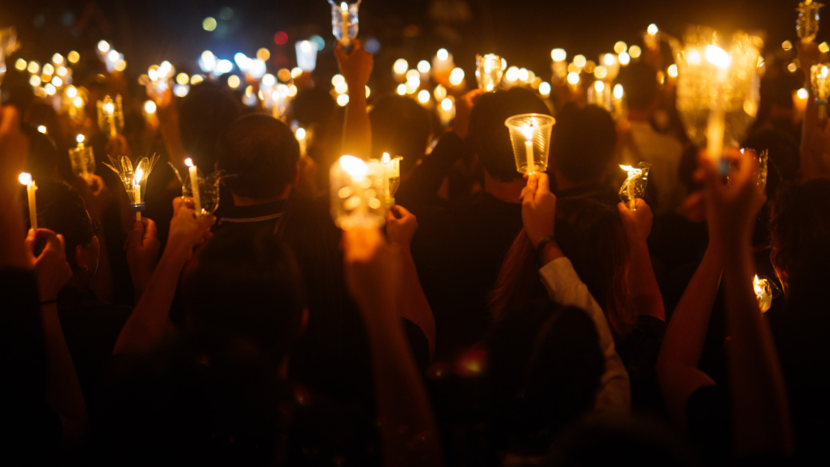 Lichtermeer: Menschenmasse ist von hinten zu sehen wie sie Nachts, Kerzen hoch hält.